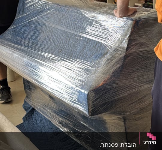 אנשים מעבירים רהיט עטוף בניילון עם עגלת גלגלים